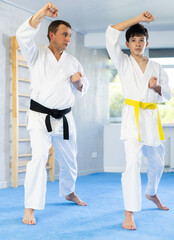Adult man and boy teenager in kimono practice karate technique in gym