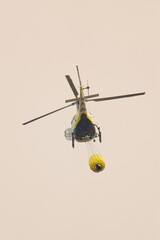Helicopter transporting water in a bambi bucket, soaring over leon, spain, while combating...