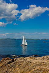Sailboat on the ocean with rocky coastline under blue sky
