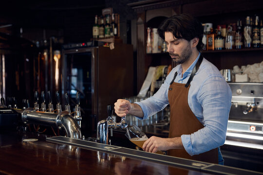 A bartender skillfully pours a beer from a tap into a glass container - Powered by Adobe