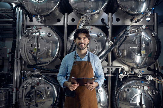 A man wearing an apron is holding a tablet inside a brewery facility