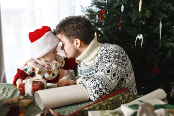 Merry Christmas! Happy father and baby son in santa hat and stylish festive sweaters wrapping...
