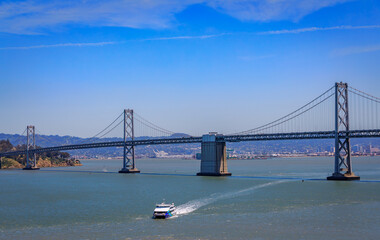 San Francisco Bay Bridge across the bay with a ferry boat on a bright sunny day