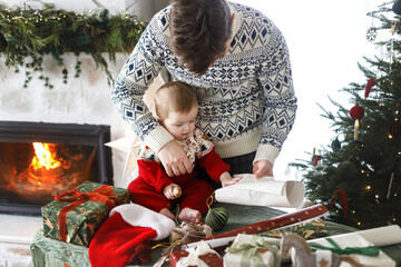 Happy father and cute baby son wrapping christmas presents on background of stylish decorated tree....