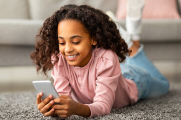 Digital natives. Positive african american teen girl using her smartphone, chatting and texting in...