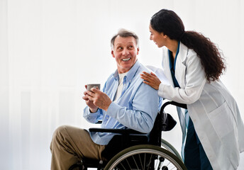 Young female doctor helping senior handicapped man in wheelchair, taking care of older male patient...