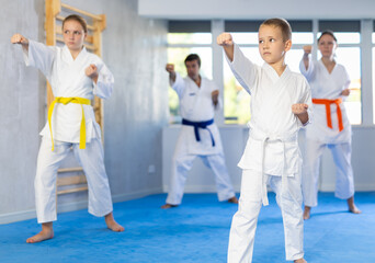 Boy and his family during practice of karate kata standing in row and closely watching man teacher,...
