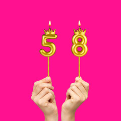 Birthday on a fuchsia background with the number 58 - Hands holding number-shaped candles