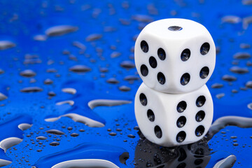 Two white dice with black dots on a blue background with water drops