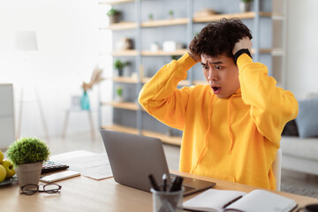 Deadline Concept. Portrait of shocked scared asian guy sitting at desk with laptop, screaming and...