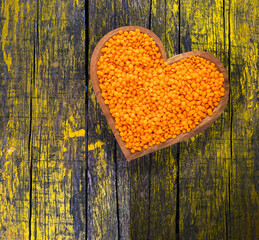 Unshelled red lentil in heart bowl - Lens culinaris.