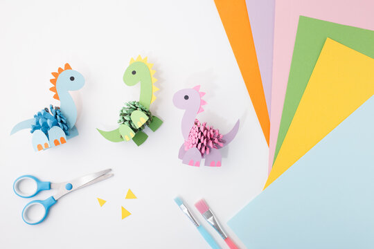 Pinecone paper dinosaurs on white background with crafting tools and materials. Ideal for educational publishers, craft supply stores, parenting content, workshops and DIY learning kits,