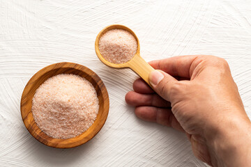 Hand holding a wooden spoon filled with pink Himalayan salt