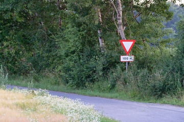 Narrow rural road by fields and woods with yield ahead warning