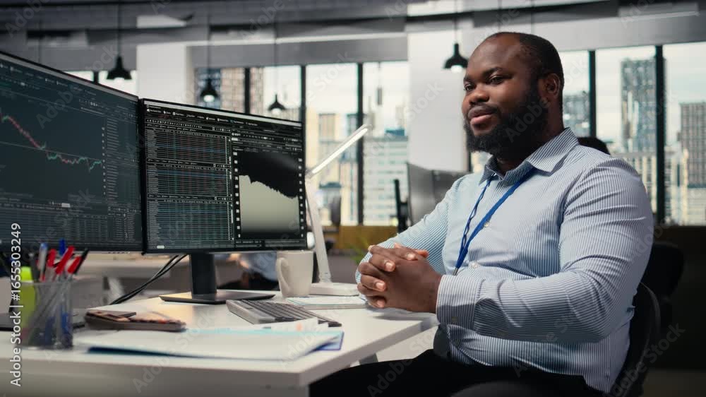 Poster smiling portfolio manager at computer desk evaluates assets based on statistics and economic indicat
