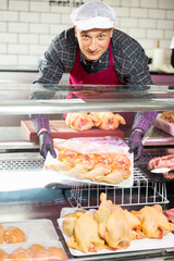 Adult male butcher sells chicken meat in butcher shop