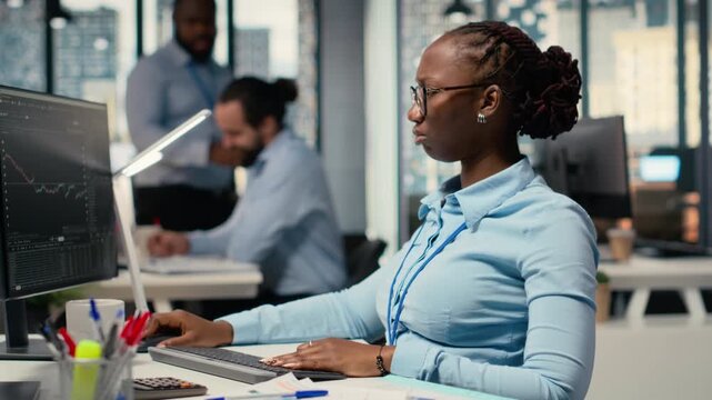 Trader frowning while looking at investment portfolio candlestick charts after unexpected market crash. African american woman upset by stock exchange account losses, camera B
