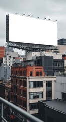 A large blank billboard on top of buildings in a city with an overcast sky and metal railing view