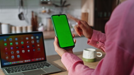 Unrecognizable woman swiping greenscreen smartphone at kitchen. Lady scrolling