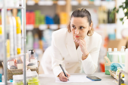 Adult woman seller conducting inventory with checklists and phone in household chemicals store