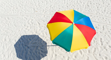 Colorful beach umbrella casting soft shadows on white sand, top view.