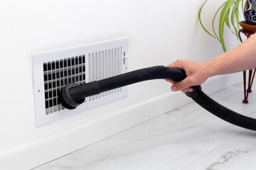 Cleaning an air vent. A person is using a vacuum to clean the air vent cover