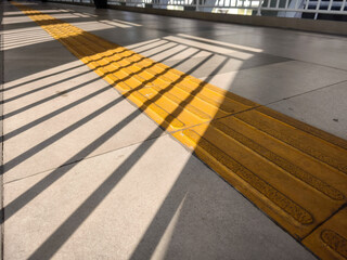 Yellow tactile paving path with shadows on pedestrian walkway