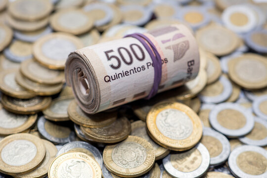 Rollo de billetes de 500 pesos mexicanos sobre una base de monedas mexicanas de 10 pesos.