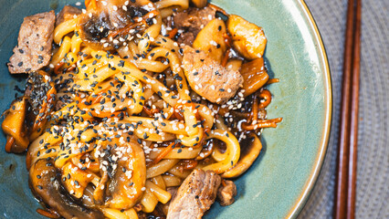 Delicious Japanese udon noodles with juicy beef, mushrooms, and carrots in a bowl. Topped with...