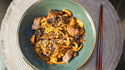 Delicious Japanese udon noodles with juicy beef, mushrooms, and carrots in a bowl. Topped with...