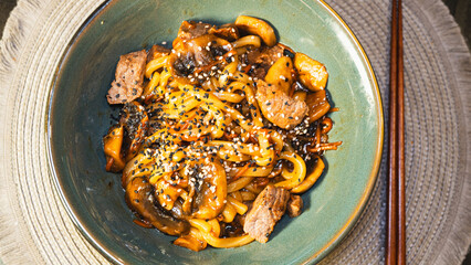 Delicious Japanese udon noodles with juicy beef, mushrooms, and carrots in a bowl. Topped with...
