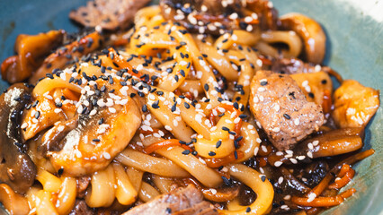 Delicious Japanese udon noodles with juicy beef, mushrooms, and carrots in a bowl. Topped with...