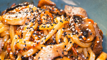 Delicious Japanese udon noodles with juicy beef, mushrooms, and carrots in a bowl. Topped with...