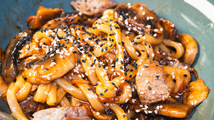 Delicious Japanese udon noodles with juicy beef, mushrooms, and carrots in a bowl. Topped with...