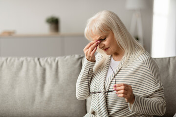 Portrait of tired mature woman massaging her nosebridge, rubbing dry irritated eyes sitting on the...