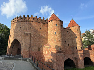 Historic brick castle with distinctive towers and crenellated walls, surrounded by greenery and...