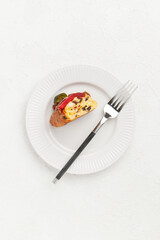 A slice of festive cake with candied fruit and nuts on a white plate with a fork placed beside it