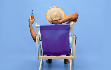 Back view of young black guy sitting in lounge chair with bottle of beer, enjoying summer vacation,...