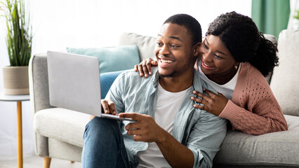 Happy young black couple shopping online at home, using laptop, copy space. Emotional african...
