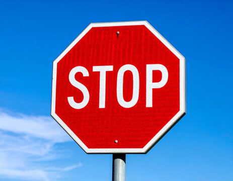 A vivid red stop sign stands prominently against a clear blue sky, symbolizing caution, control, and road safety. Red Stop Sign Against Bright Blue Sky.