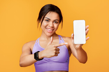 Sports application. Excited black lady holding and showing smartphone, indicating at black empty...