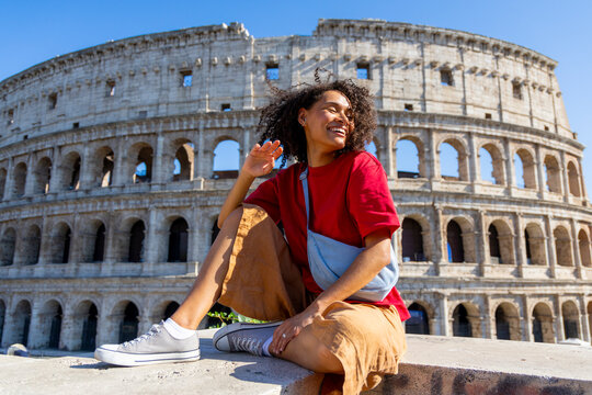 A cheerful and vibrant young woman strikes a pose in front of the iconic Colosseum in Rome, proudly showcasing the stunning beauty and grandeur of this ancient landmark that attracts many tourists