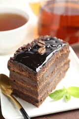 Piece of chocolate cake served with mint, spoon and tea on table, closeup