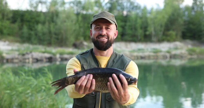 Smiling fisherman holding caught fish near lake at summer