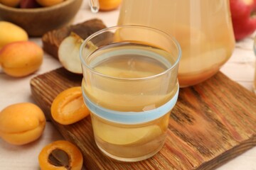 Tasty compot in glass and fresh apricots on table, closeup