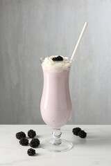 Tasty blackberry milkshake with whipped cream in glass and berries on white marble table
