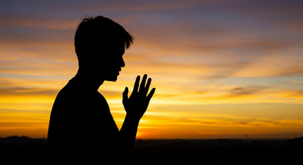 Silhouette of a person with hands clasped in prayer against a vibrant sunset backdrop in golden hues vreated with genrated ai