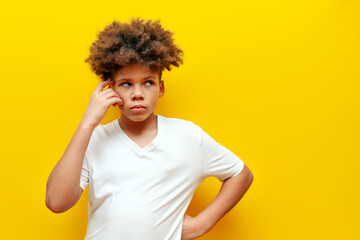 African American puzzled teenage boy in white t-shirt thinking and doubting on yellow isolated...
