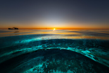 Sunset over Heron Island in Queensland with golden light reflecting on the glassy surface of the...
