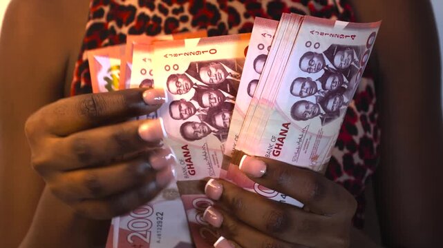 Black African young lady in red,nude,black colourful dress counting 200 ghanaian cedis notes to the camera - Powered by Adobe
